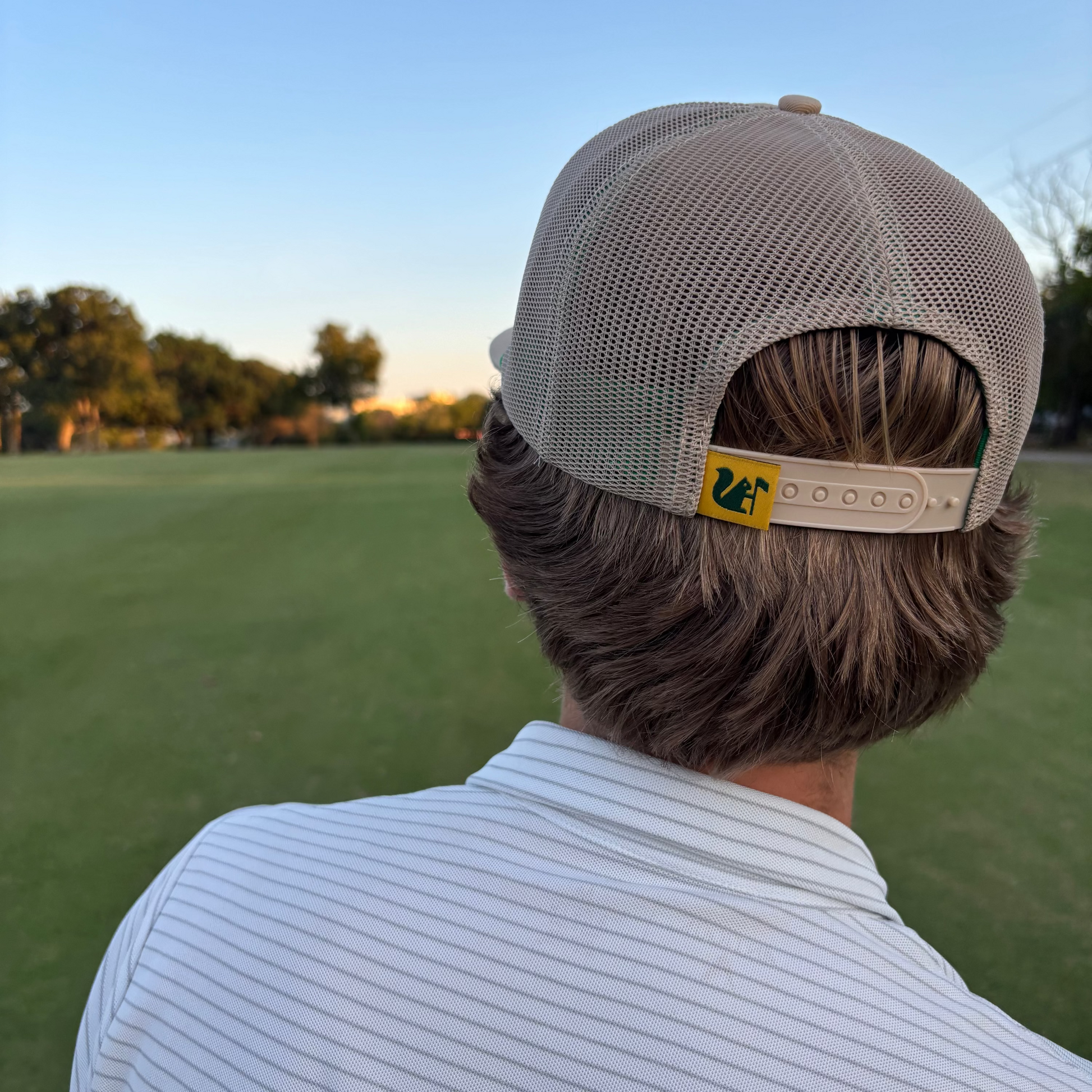 Person wearing a beige cap with a logo on a grassy field